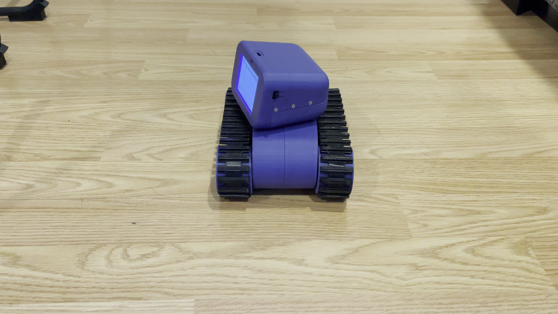 The Treads Robot turns across a wood floor while its screen shows the program it is running